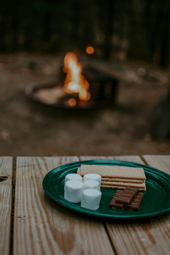 S'mores setup with marshmallows, graham crackers, and chocolate by a campfire.